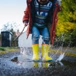 A picture of a young child enjoying jupingin muddy puddles.