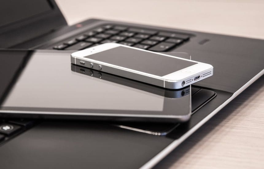 Pile of digital technology with a tablet and mobile phone on top of an open laptop